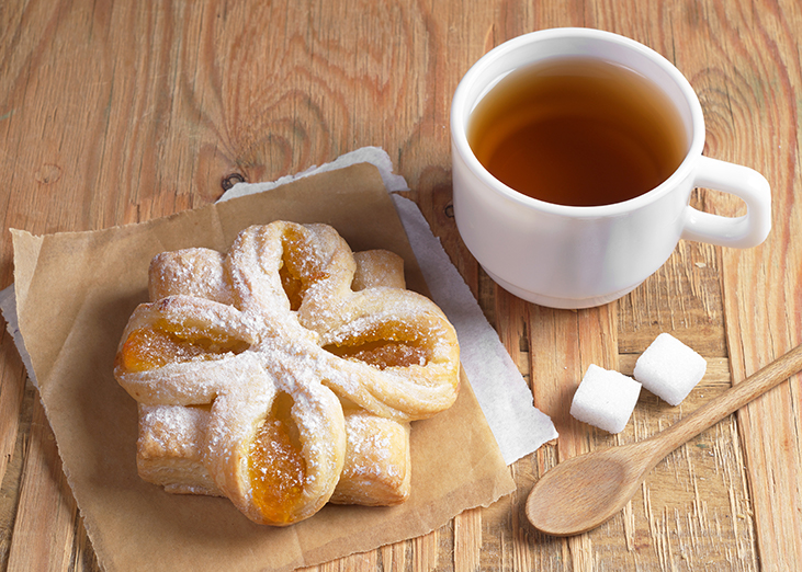 apple filled spring danish on a napkin next to a mug of tea