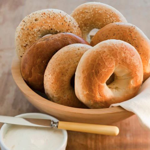 A brown bowl filled with bagels with a side of cream sheese