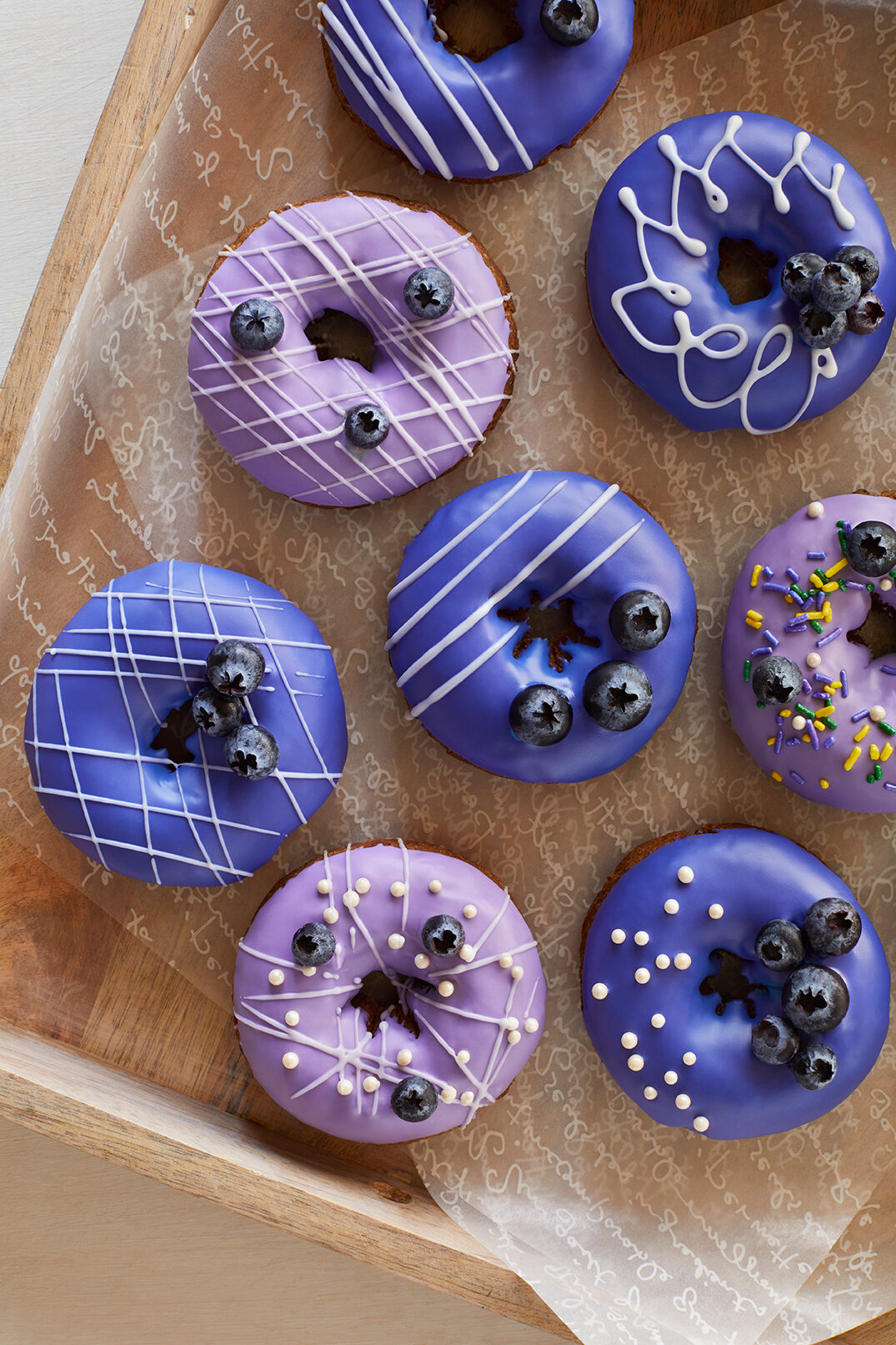 overhead shot of frosted Purple blueberry cake donuts on parchment paper