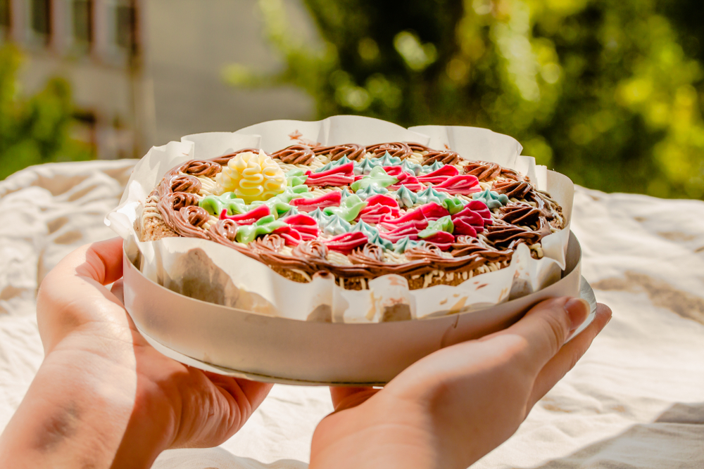 Hands holding a finished decorated cake in a cake tin with a cake pad