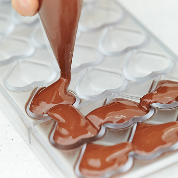 A pastry bag full of chocolate filling up heart molds