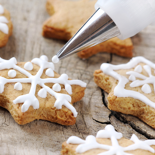 A pastry bag with a small frosting tip decorating snowflake cookies