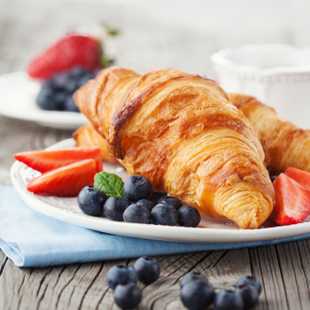 croissant featuring laminated dough on a plate with a side of fruit