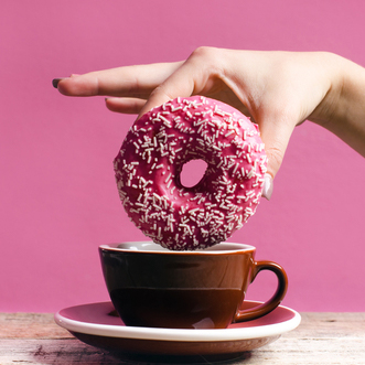 a hand holding a pink donut with sprinkles above a copy of coffee