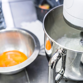 Egg yolks in a bowl next to an industrial mixer whipping egg whites