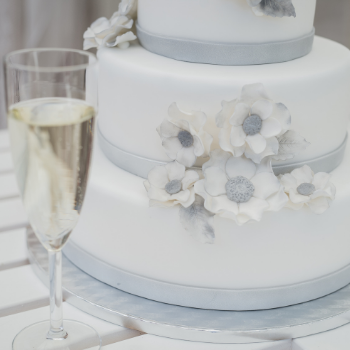 A wedding cake decorated with fondant with a glass of champagne on the side