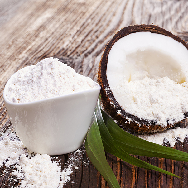 A bowl of coconut flour next to a freshly opened coconut