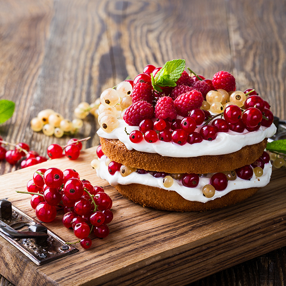 A fruit cake with layers of whipped topping and fruit on a cutting board