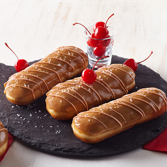 Maple glazed donuts topped with cherries on a black surface