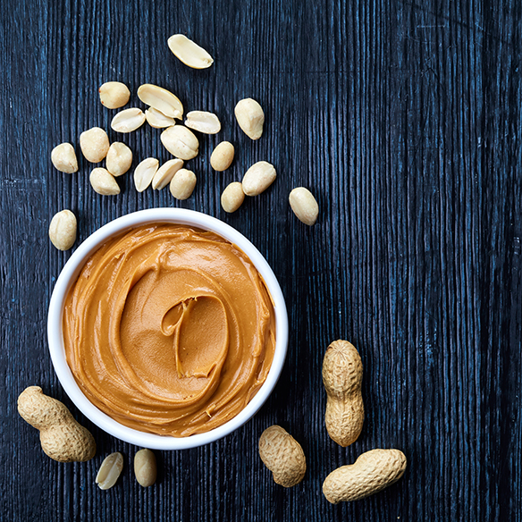 overhead peanut butter in a white bowl surrounded by peanuts