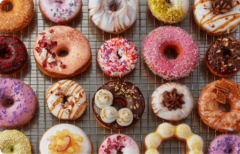 an overhead shot of a variety of glamorously decorated donuts on a wire rack