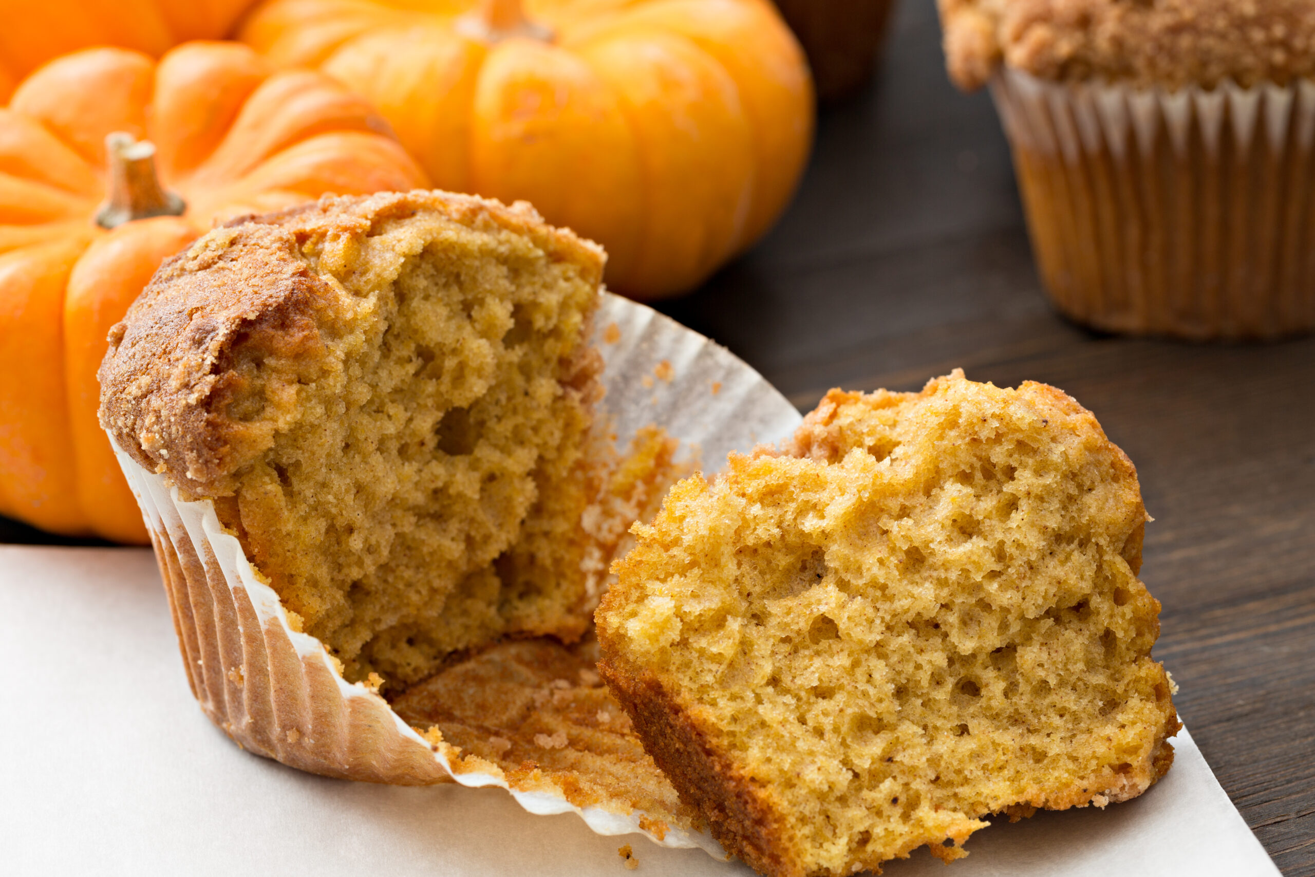 A high angle, extreme close up horizontal photograph of a torn open pumpkin muffin with several small pumpkins in the background.