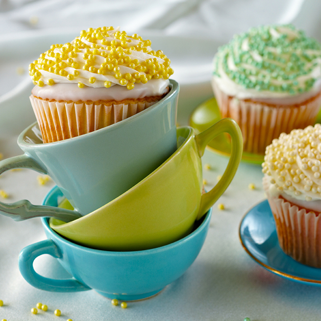 A stack of teacups topped with a cupcake decorated with pearls